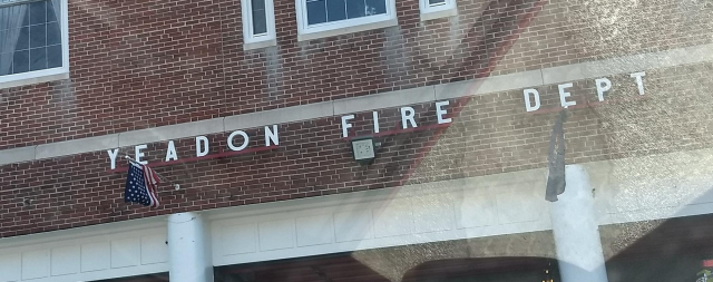 A portion of the vehicular
entrance of the
firehouse, which is a three-story brick-faced building displaying the
flags of the U.S. and of Pennsylvania.  Bolted to racks above the main
driveways are the letters YEADON FIRE DEPT.