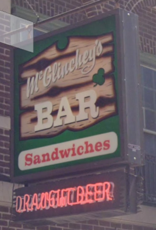 Street view of the sign outside McGlinchey's.  At the top it says
“McGlinchey's Bar” with a green shamrock.  Under this in clear red
letters on white is the word “Sandwiches”.  Below this hands a red
neon sign that reads “DRAFT BEER”.