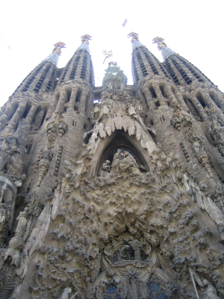 The Nativity façade, as seen
from the ground, looking up.  On each side of the façade are two tall,
curved spires, somewhat resembling the congealed wax on the outside of
a candle. <br />
Each is decorated with sculpture columns, and windows and other
perforations.  Far above the spires end with huge red and yellow
flowers or medallions.