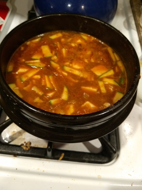 Soondubu in the
bot on the range.  The  pot is dark-glazed heavy earthenware.  The
soondubu is a dark-red soup (from the chili paste) full of floating
pieces of white dubu and green-edged zucchini.