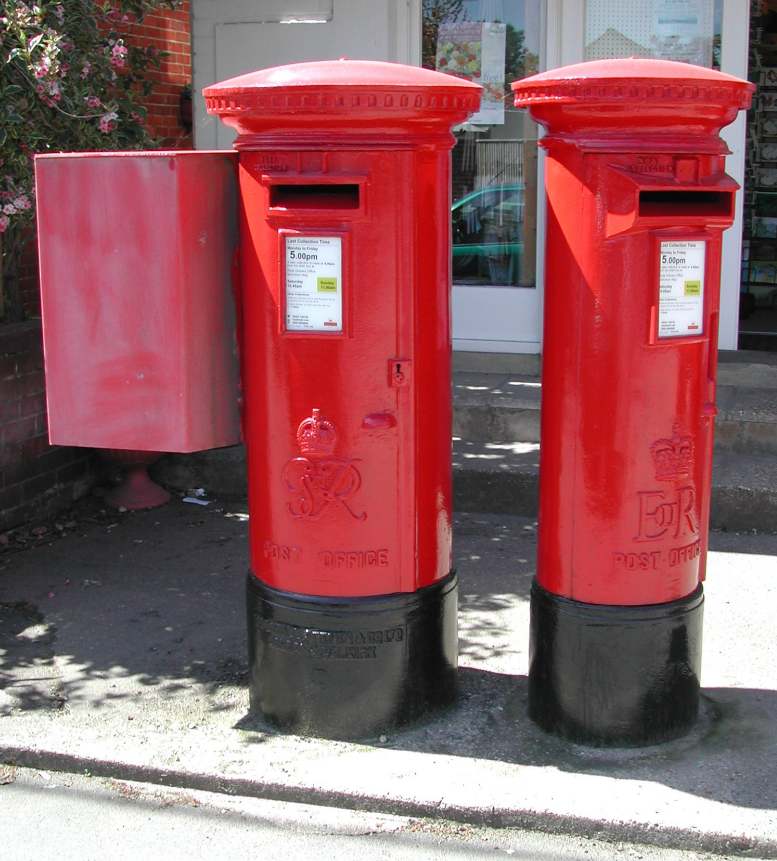 A
photograph of two red pillar-style post boxes, side by side.  Each is
roughly cylindrical, with a black base, a flat flaring top, and a
large slot near the top for the insertion of letters.