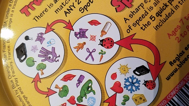 The back of the 'Spot It' box shows four white circular cards,
each with 8 little pictures on it. A red double-headed arrow between
the first two cards shows that both cards have a picture of a
ladybug.  Another arrow between the second and third cards shows that
both cards have a picture of a red heart.  The next arrow connects the
trees on cards 2 and 3, and a fourth arrow shows that cards 1 and 4
both have apurple cat.  Even though part of card 3 is cut off, we can
see that they share a pair of lips. Cards 2 and 4 both have a gray
padlock picture, even though there's no arrow pointing it out.