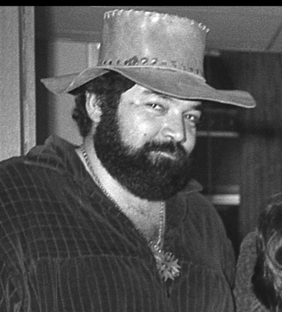 Paul L. Smith
is a heavyset, slightly overwight man with a thick, curly black beard
and mustache.  In this (grayscale) picture his shirt, which appears to
be velour, is open at the neck, dispolaying a necklace with a large
star resting among a profusion of curly black chest hair.  He is
wearing a battered leather hat with a wide brim, and is looking
sidelong at the camera, with a smile of amusement.