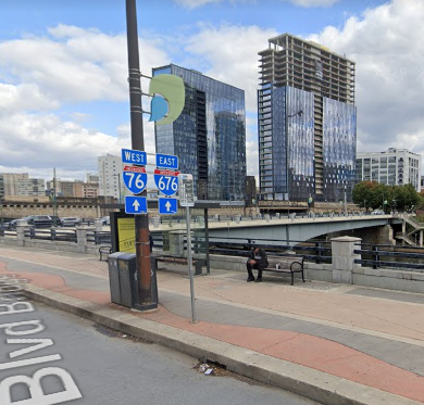 Street view of Philadelphia. In the center is a lamp post with two red and blue Interstate highway shields affixed, indicating that entrances to I-76 West and I-676 East are ahead.