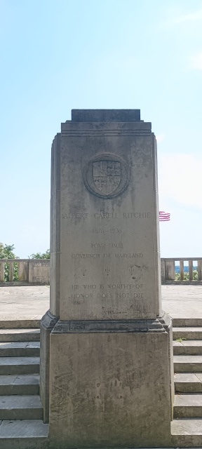 A sandstone plinth with the Maryland state coat of arms carved in bas-relief at the top. Under this are engraved words: ALBERT CABELL RITCHIE / 2876 – 1936 / FOUR TIMES GOVERNOR OF MARYLAND / HE WHO IS WORTHY OF HONOR DOES NOT DIE.