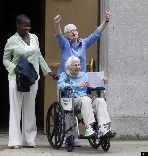 Two elderly women with white
hair, both smiling.  One is seated in a wheelchair, holding up an
official-looking certificate.  The other has her arms raises in
triumph.  A third woman stands beside them, smiling.