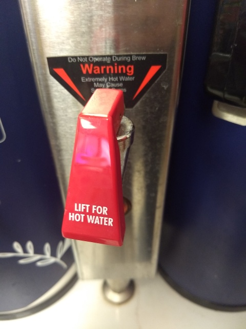 A red plastic handle on a
coffee brewing station with the words “LIFT FOR HOT WATER”