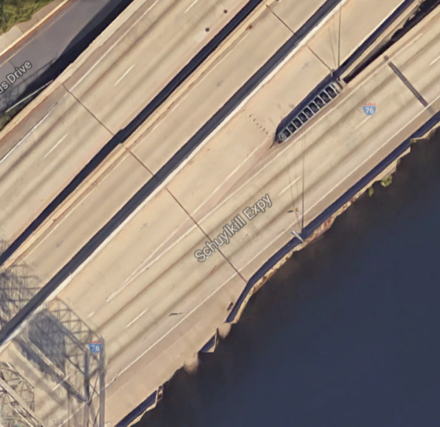 Satellite view of a highway exit,
labeled “Schuylkill Expy”.  Traffic flow is from lower left to upper
right, with one road splitting to become two.  The entering road is
three lanes, and the left lane diverges and goes up a ramp while the
other two lanes continue in the same direction. The space between the
two lanes, before the roadway actually splits, is a long, narrow
triangle shape.