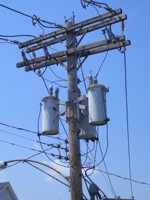 A wooden power utility pole,
including cobra-head street light,
with three large gray cylinders mounted on it under the main
wires